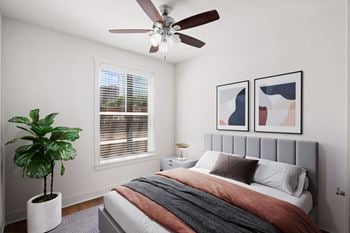 A bedroom with a bed, a ceiling fan, and a potted plant.